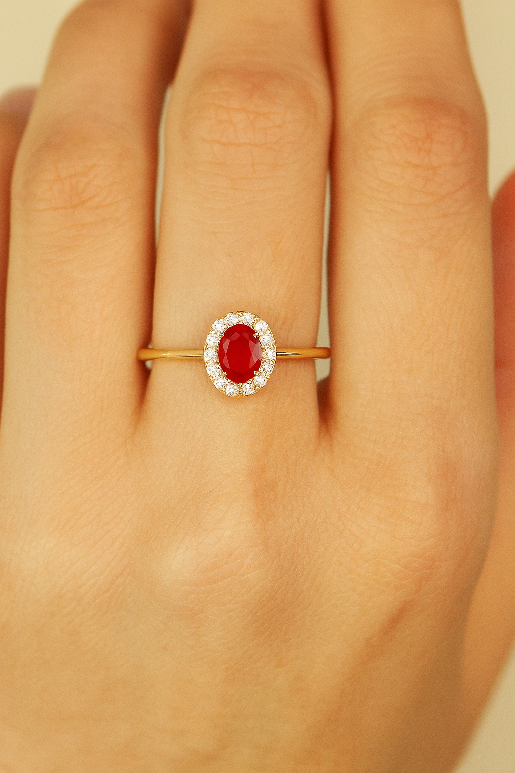 Gold ring with a red gemstone on a hand against a neutral background