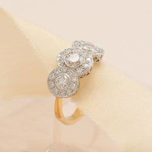 Vintage style engagement ring set with three round brilliant cut diamonds in a bezel setting surrounded by smaller diamonds 
