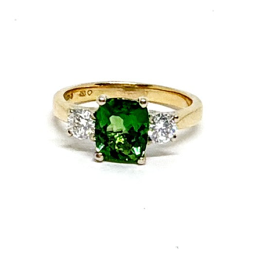A yellow gold ring featuring a large cushion-cut green gemstone in the center, flanked by two small round clear stones on a white background.
