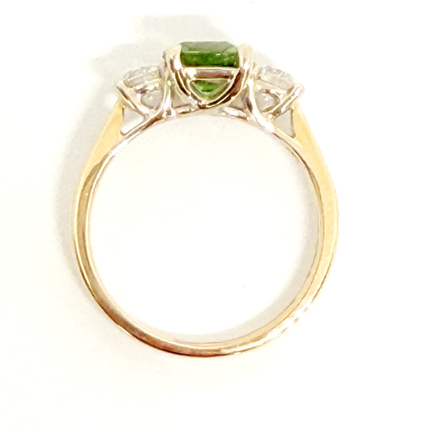 A yellow gold ring featuring a central green rectangular gemstone and two small clear accent stones on either side, shown against a plain white background.